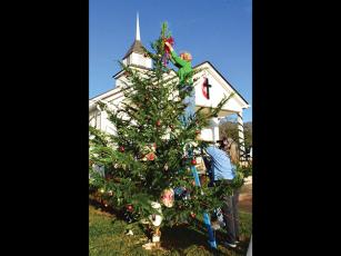 Press photo/Linda Mathias - Sally Williams puts a ribbon at the top of the Hickory Knoll United Methodist Church’s first Christmas tree as pastor Stephanie Thompson steadies the ladder. Hickory Knoll will have an outdoor Christmas Eve service at 8 p.m.