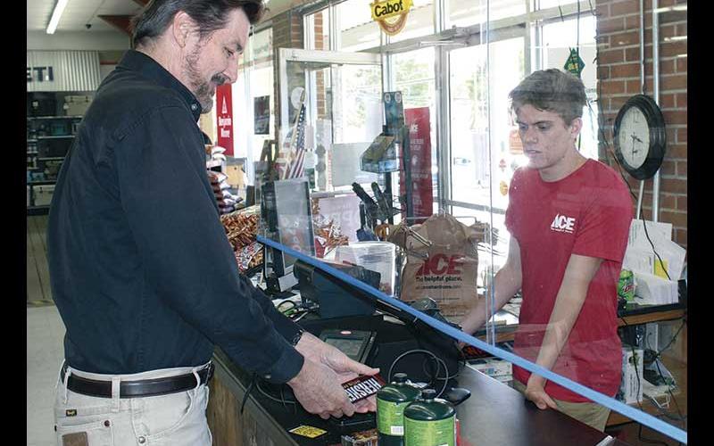Liam Graham rings up Steve Wilcox’s purchase at Appalachian ACE Hardware from the other side of a sneeze guard.