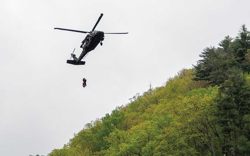 Photo/Bob Scott - A National Guard helicopter was called in to help rescue a man who had fallen down the California Mountain side of the Cullasaja Gorge. After lifting the man from the side of the mountain, the helicopter then returned to lift the rescue workers who had repelled down the mountain.