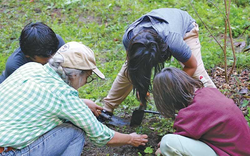 Photo submitted - Noquisi Initiative Executive Director Elaine Eisenbraun plants perennial shrubs and ground cover for the Cherokee Food Forest with K-6 students from New Kituwah Academy.