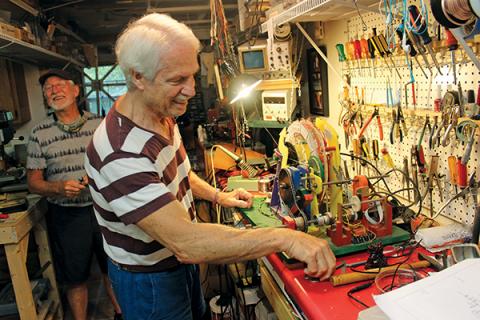 Press photo/Linda Mathias - Andrew Latorre shares a laugh with Tom Tyre as he works on the mechanical Democracy Machine at their home in Otto.