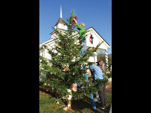 Press photo/Linda Mathias - Sally Williams puts a ribbon at the top of the Hickory Knoll United Methodist Church’s first Christmas tree as pastor Stephanie Thompson steadies the ladder. Hickory Knoll will have an outdoor Christmas Eve service at 8 p.m.