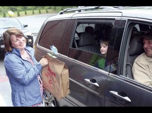 Press photo/Jake Browning - First-grader Lawson Clay, accompanied by his father Jason Clay, picks up his graduation goodie bag from teacher Pam Owens at East Franklin Elementary School’s farewell parade.