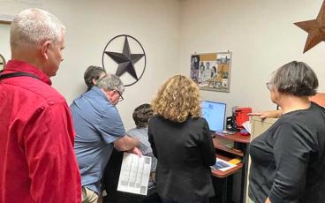 Press photo/Mia Overton - Macon County Board of Elections board members and staff watch the new voting equipment tabulate the ballots on Tuesday night.
