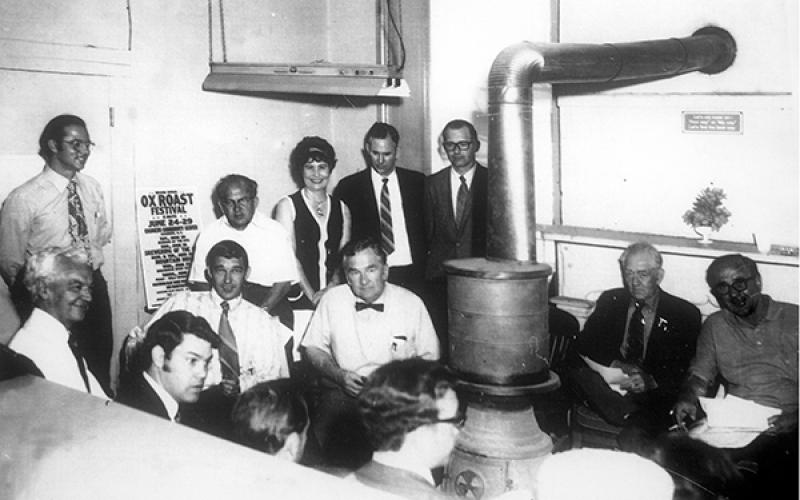County commissioners and other local officials meet around a pot-bellied stove in the old courthouse in this photo from about 1970. That’s Dick Jones standing by the stovepipe, next to Sheriff George Moses. Press editor Bob Sloan is standing to the right of a poster for an Ox Roast Festival. County manager Ron Winecoff is in front of Sloan and County Chairman Oscar Ledford is sitting beside him. Also shown are the two other county commissioners and members of the Highlands town board. 