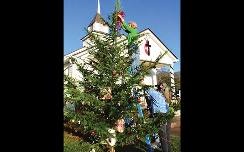 Press photo/Linda Mathias - Sally Williams puts a ribbon at the top of the Hickory Knoll United Methodist Church’s first Christmas tree as pastor Stephanie Thompson steadies the ladder. Hickory Knoll will have an outdoor Christmas Eve service at 8 p.m.